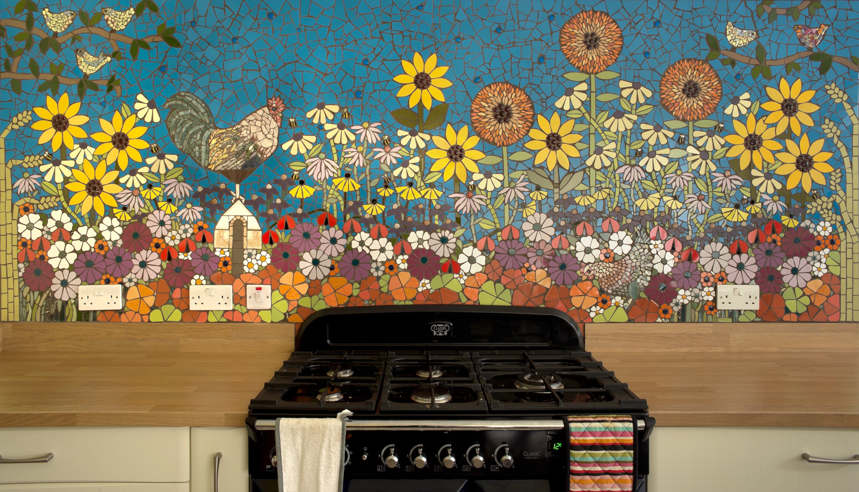 colourful mosaic above a cooker and kitchen units representing flowers and a cockerel