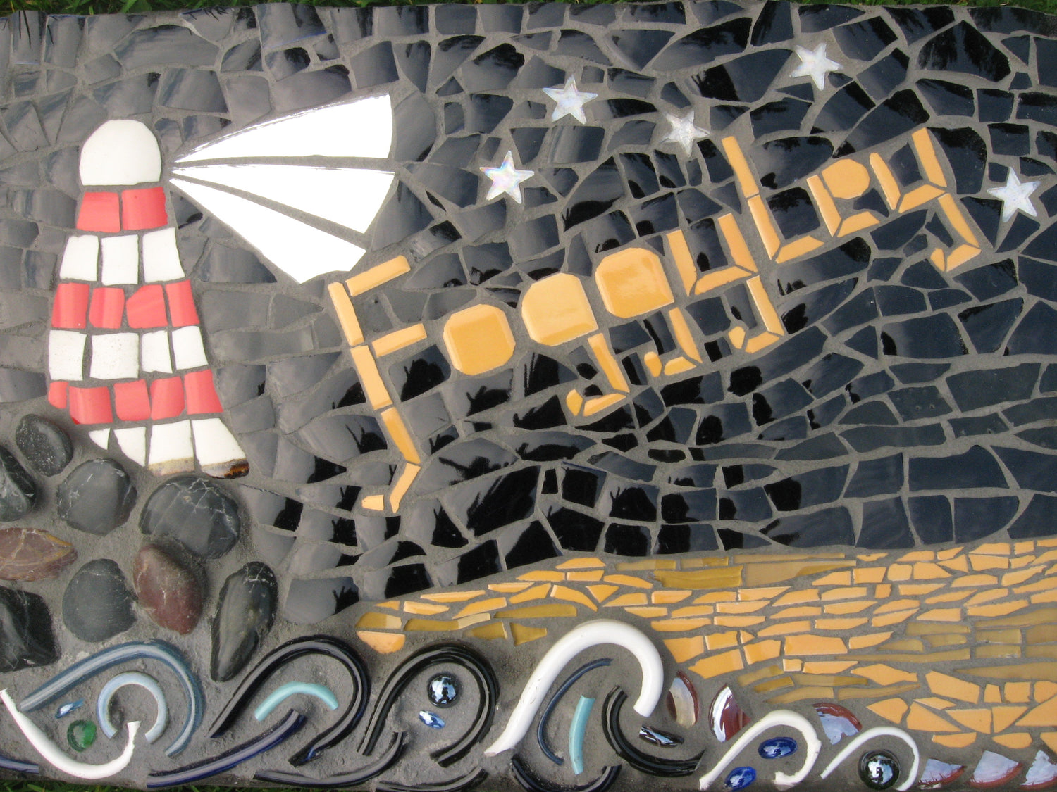 A lighthouse and stormy sea is in mosaic, with Foggyley written in the sky