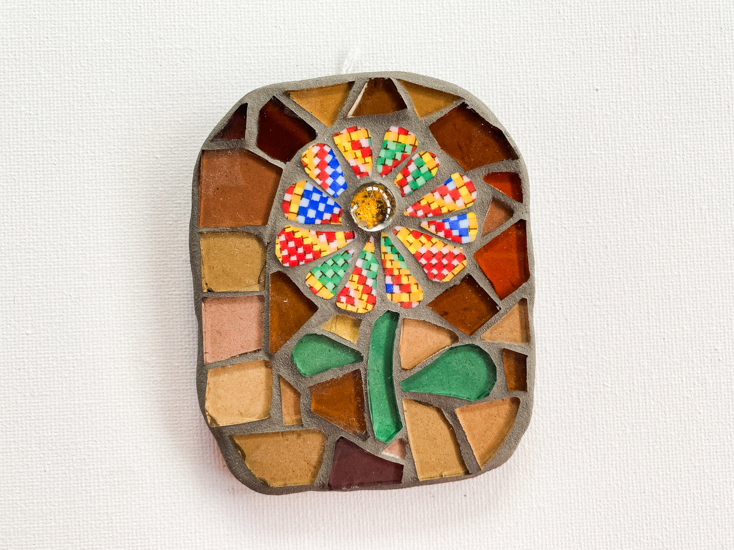 Small mosaic of multi-coloured petaled flower with brown glass background, photographed on white