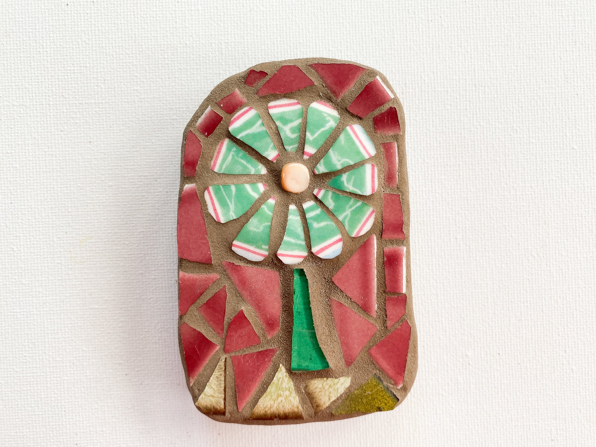 Small mosaic of green petaled flower with pinky red tile background, photographed on white