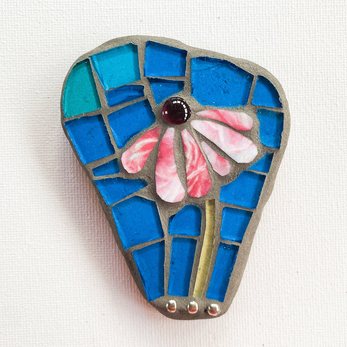 Small mosaic of pink petaled flower with blue glass background, photographed on white