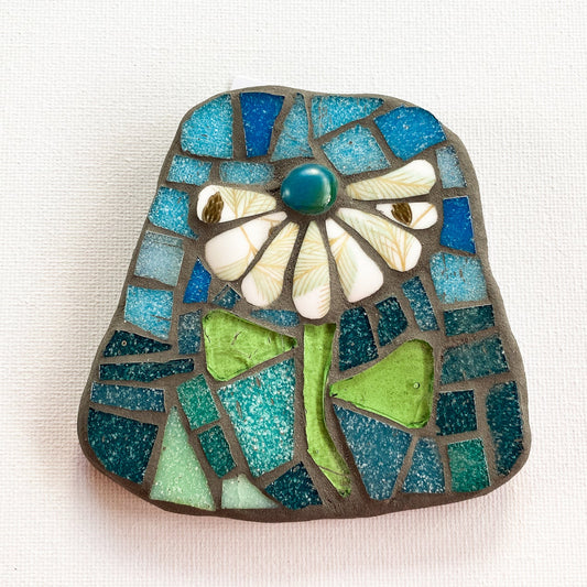 Small mosaic of patterned cream petaled flower with mixed blue tile background, photographed on white