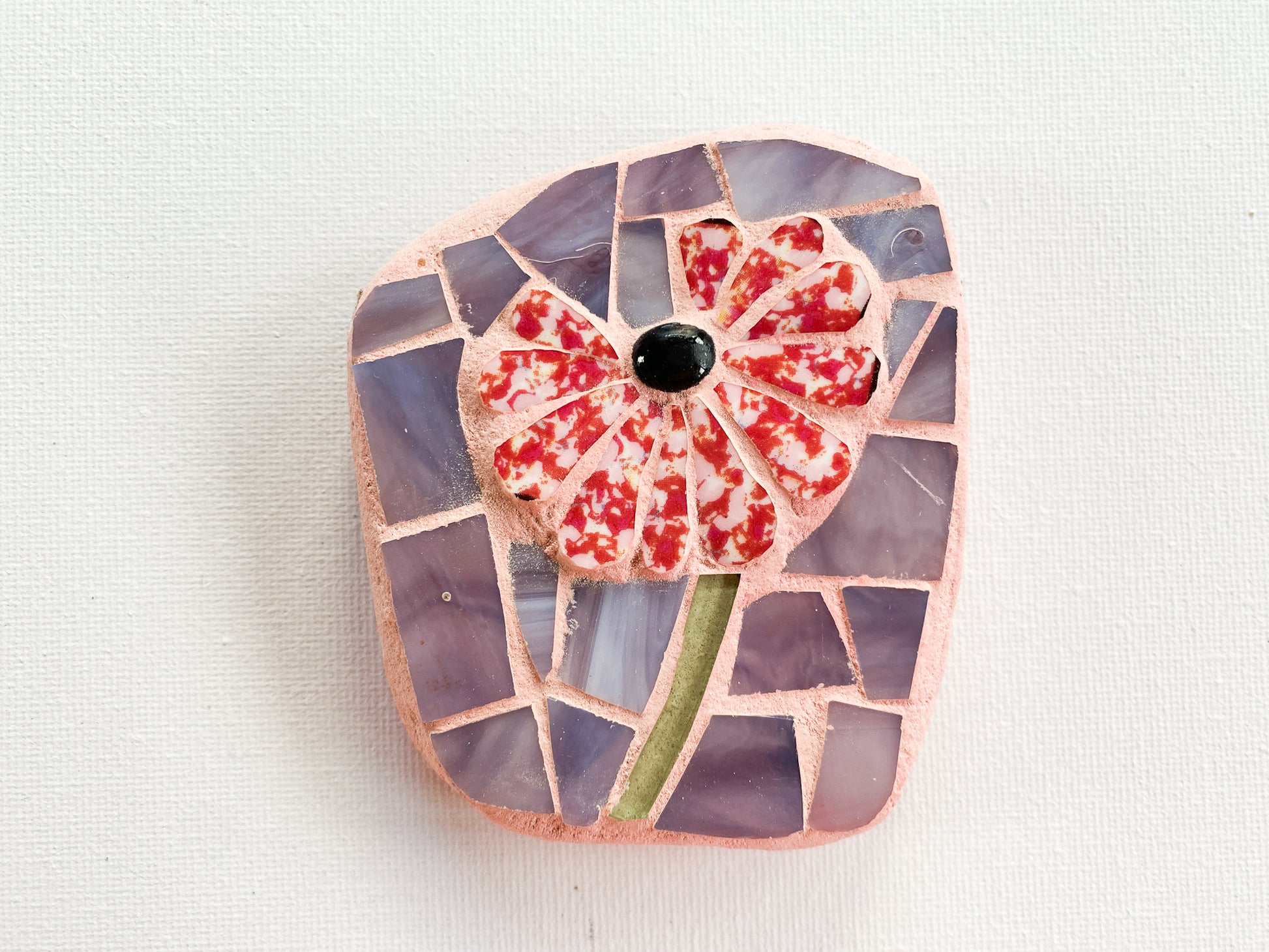 Small mosaic of red and white petaled flower with purple glass background, photographed on white