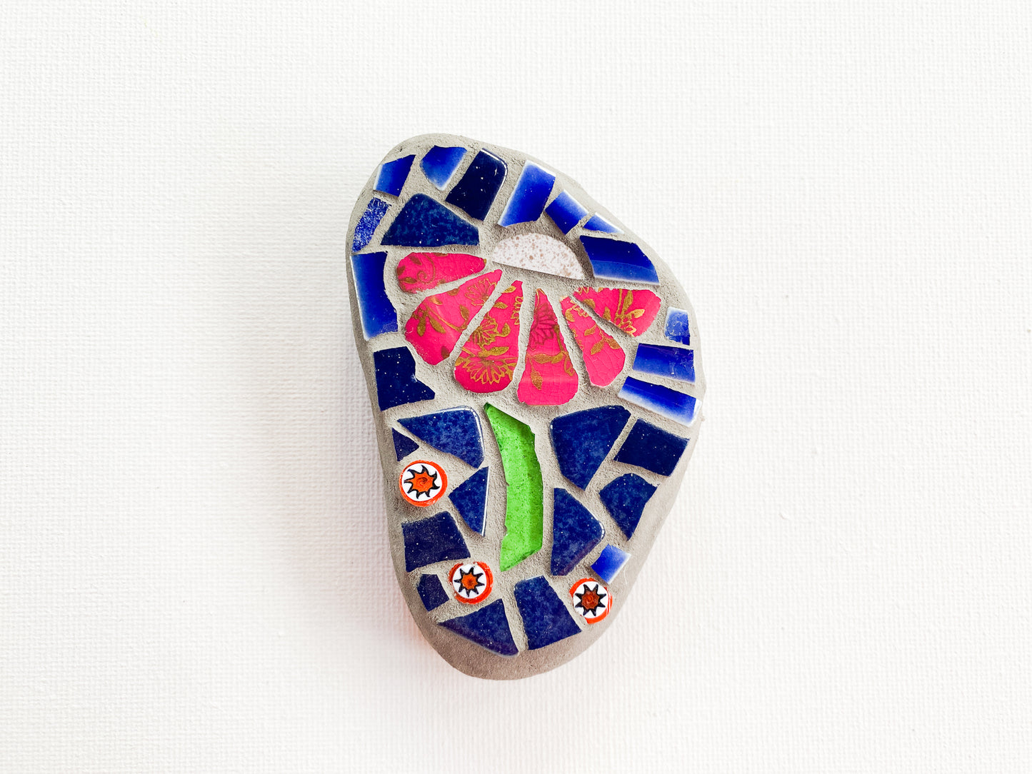 Small mosaic of pink petaled flower with blue tile background, photographed on white