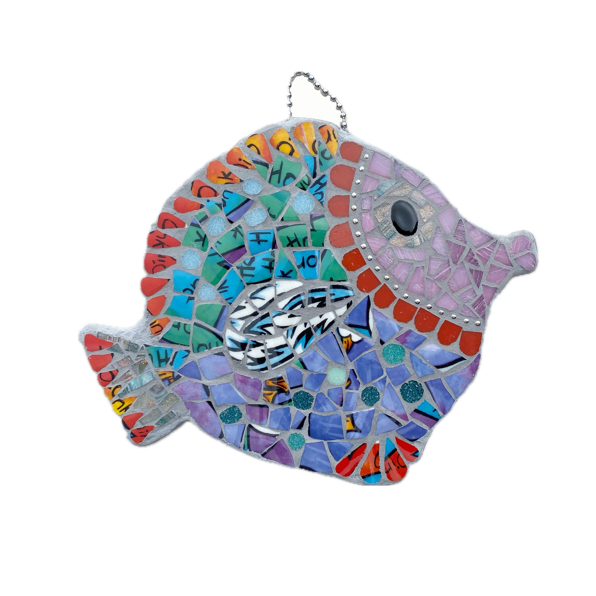 A mosaic fish made from bright purple and turquoise crockery, pink face surrounded by ball chain and curved red tiles.  Fins and tails are in a red china.  Hangs by a ball chain at the top.  Photographed on a white background