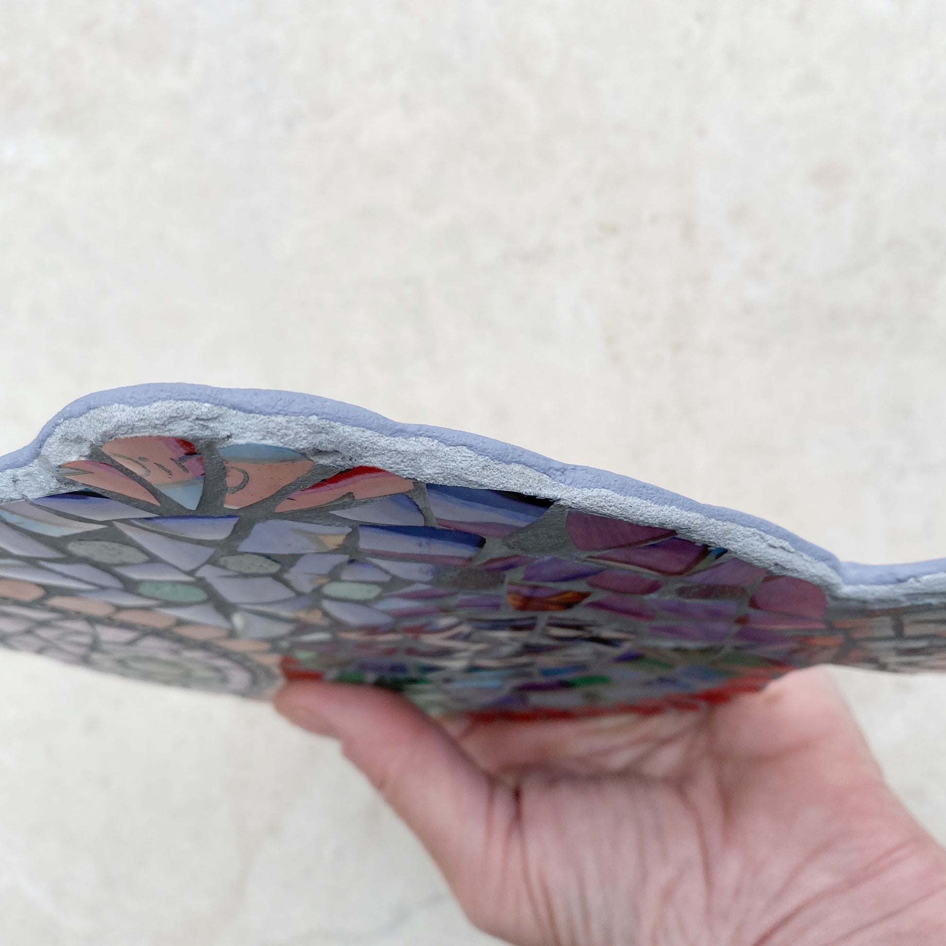 A mosaic fish made from bright purple and turquoise crockery, pink face surrounded by ball chain and curved red tiles.  Photographed showing the depth of the mosaic