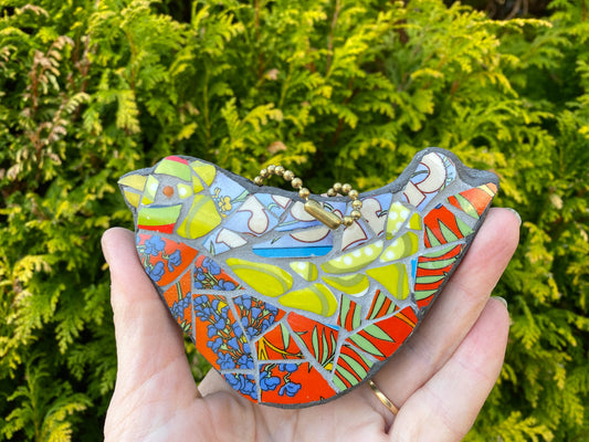 A colourful mosaic bird with red breast, and green head and wings, made from broken crockery.  Shown hand held