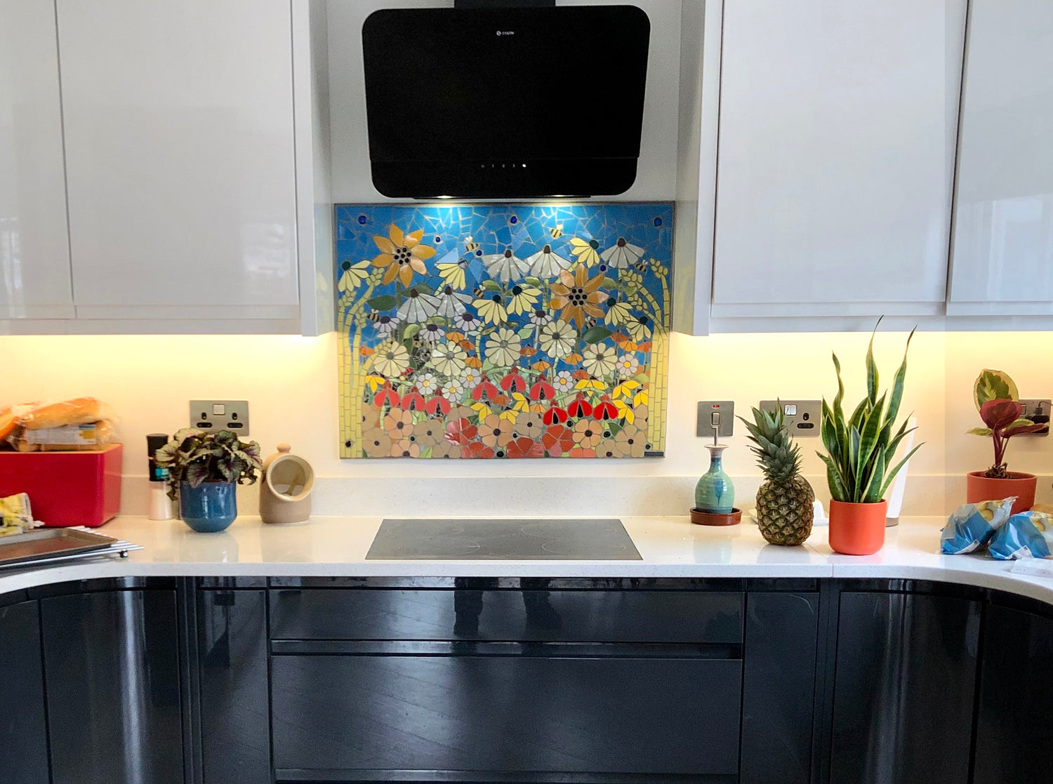 colourful mosaic splashback of flowers with a black cat above a hob with white kitchen units