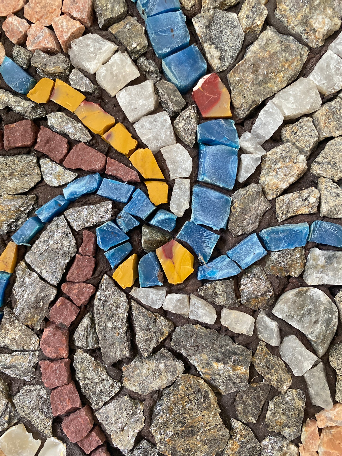Close up of a circular mosaic made of various stones, with threads of blue and yellow plastic, and quartz