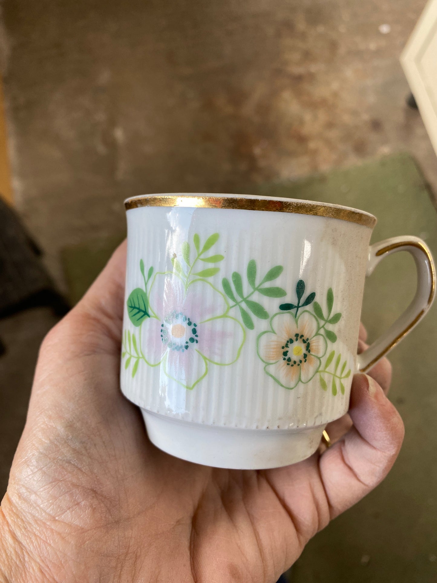 Hand holding a floral-patterned mug with gold trim against a blurred background