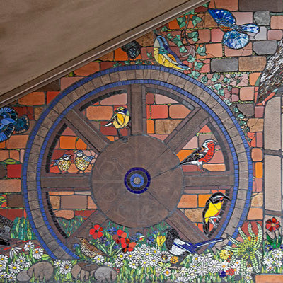 a wagon wheel against a brick background surrounded by birds executed in mosaic