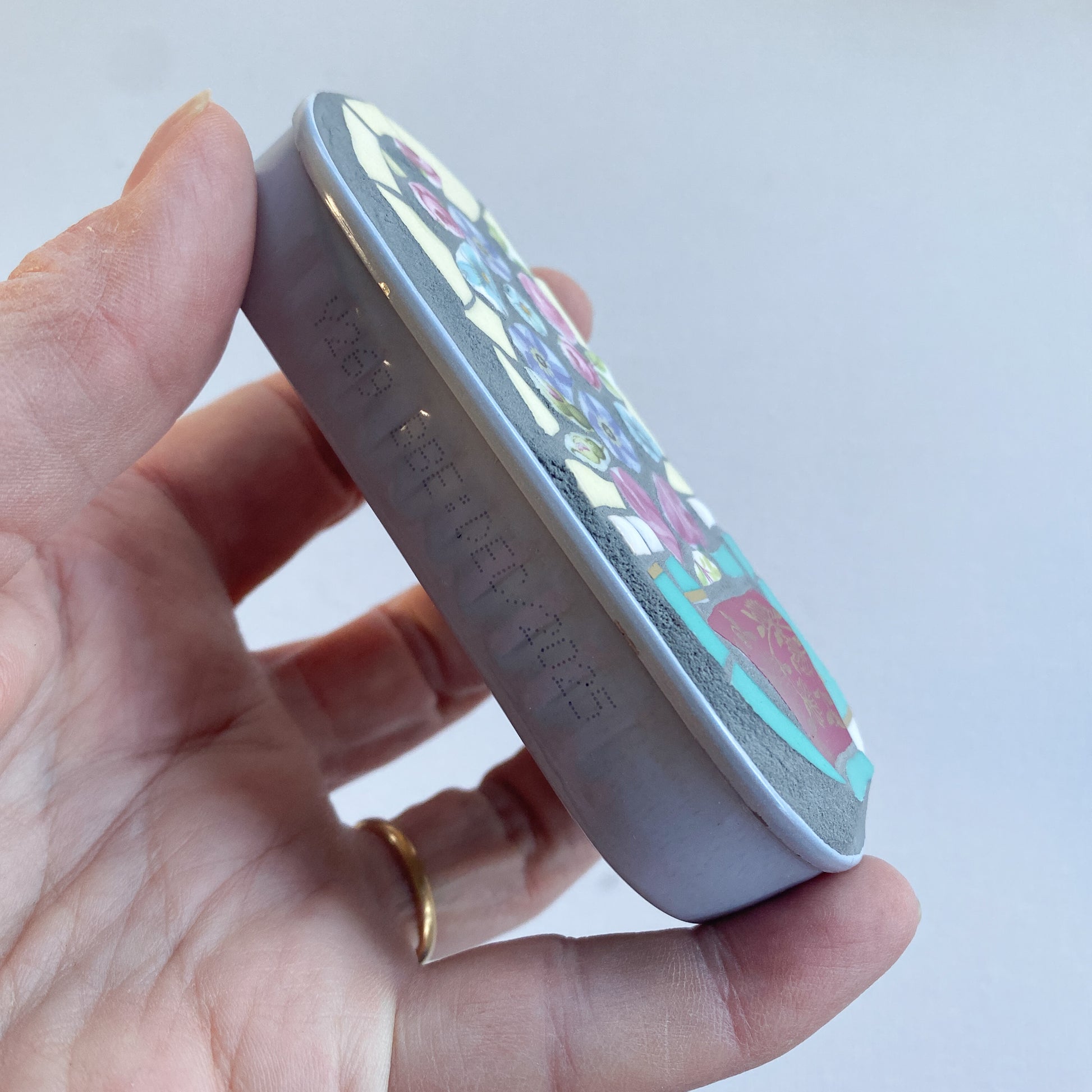 Hand holding a mosaic made in an anchovy can with a plain background