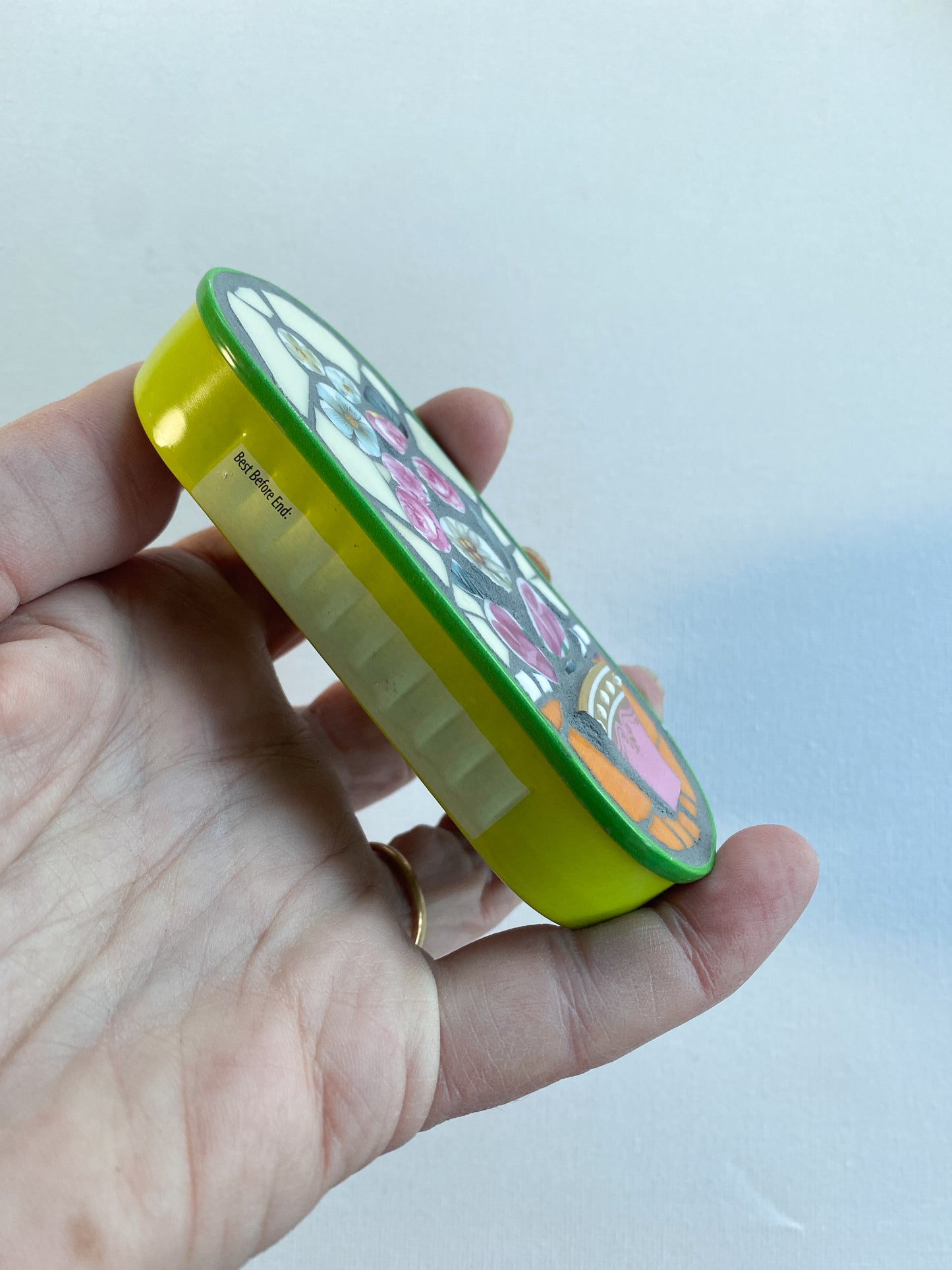 Hand holding a mosaic made in a lime green anchovy can with a plain background