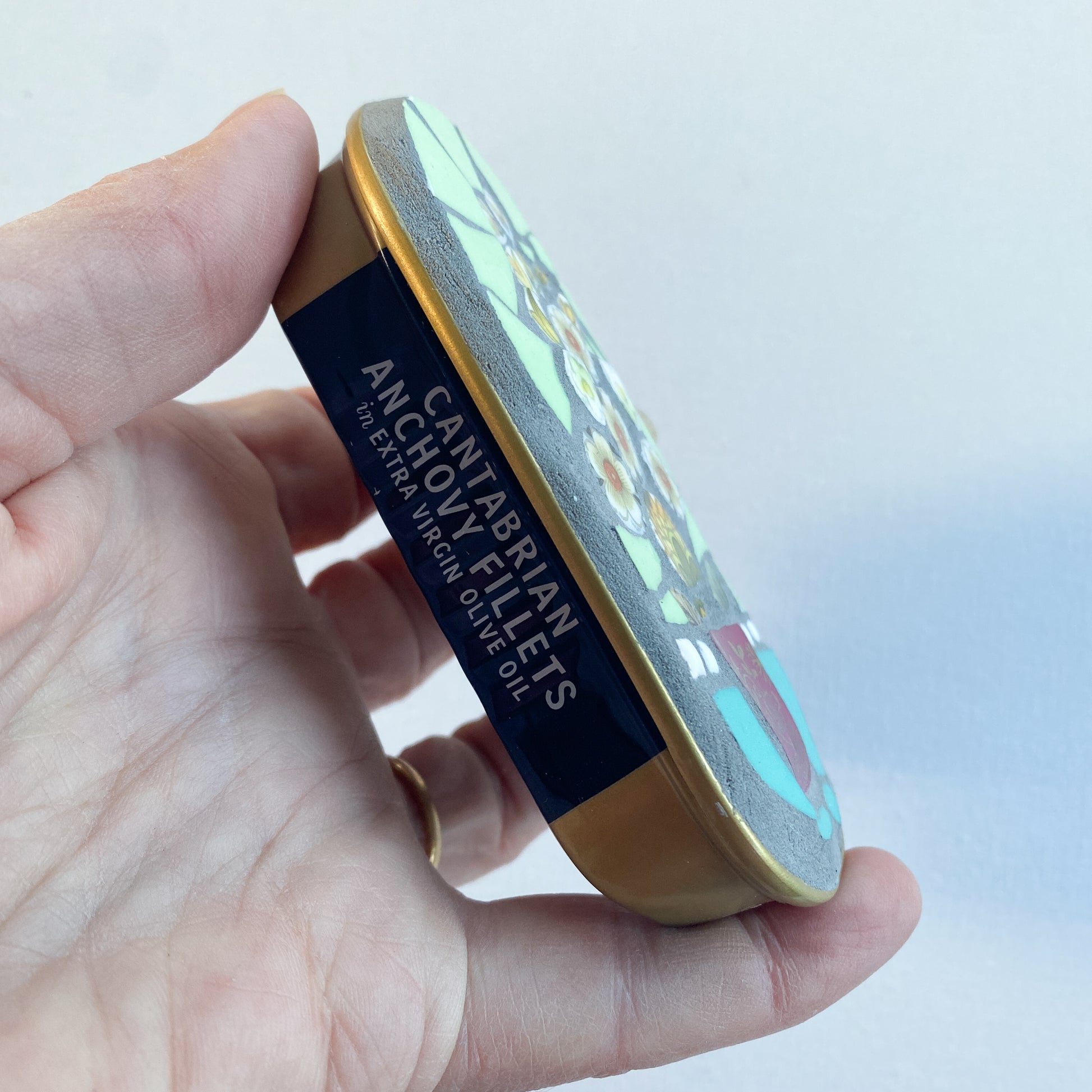 Hand holding a mosaic made in an anchovy can with a plain background