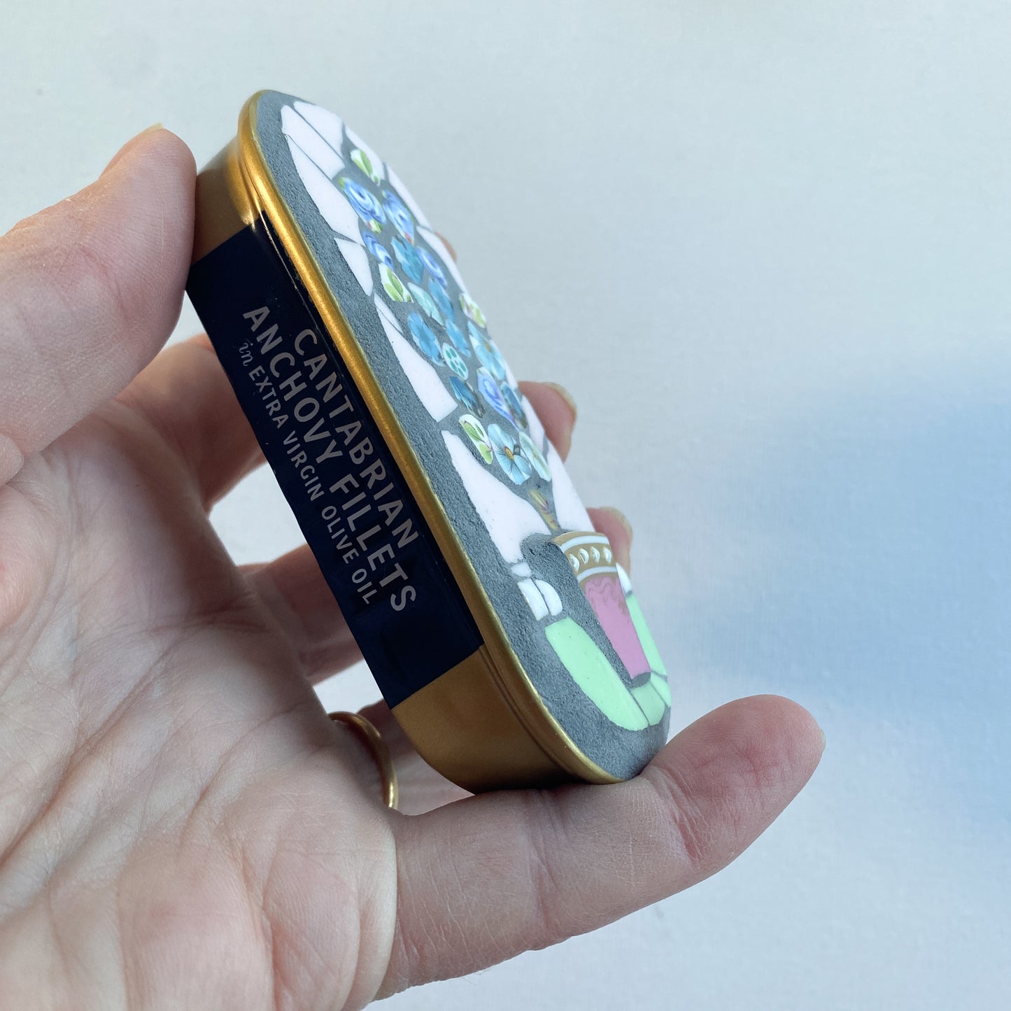 Hand holding a mosaic made in an anchovy can with a plain background