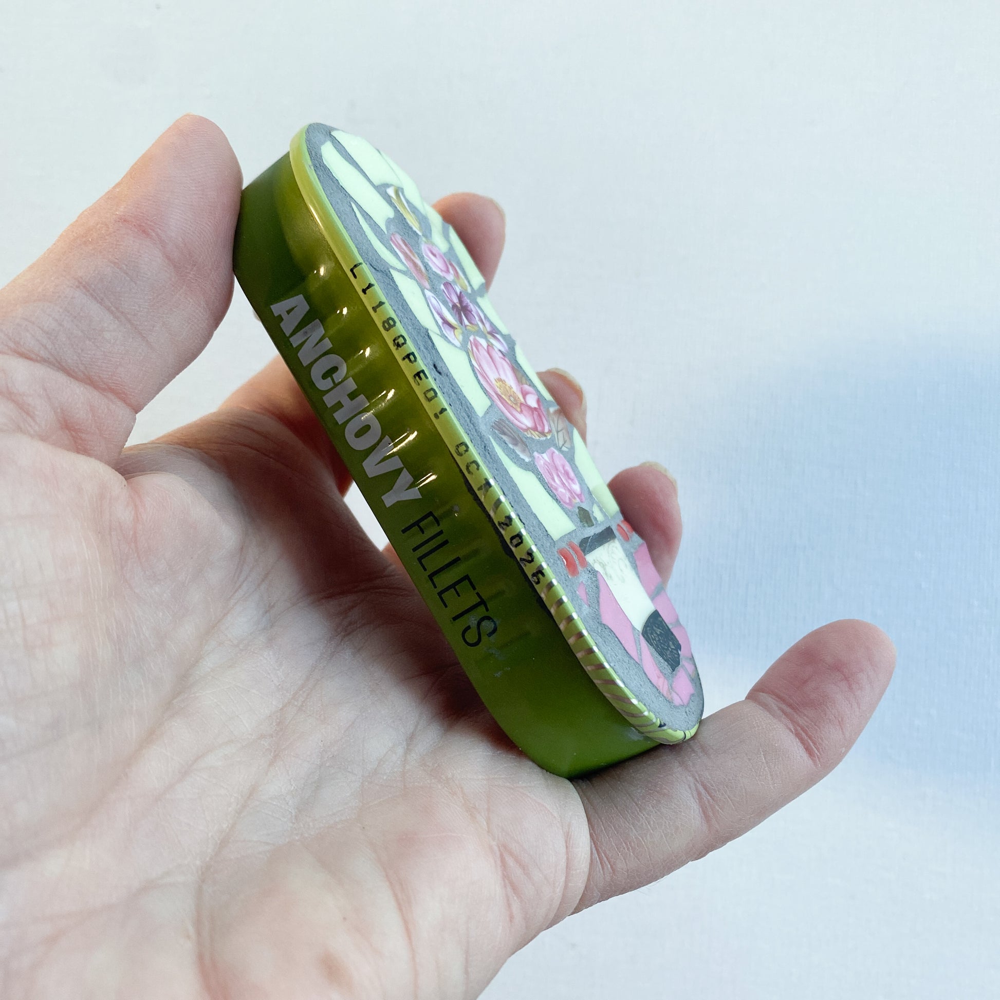 Hand holding a mosaic made in an anchovy can with a plain background