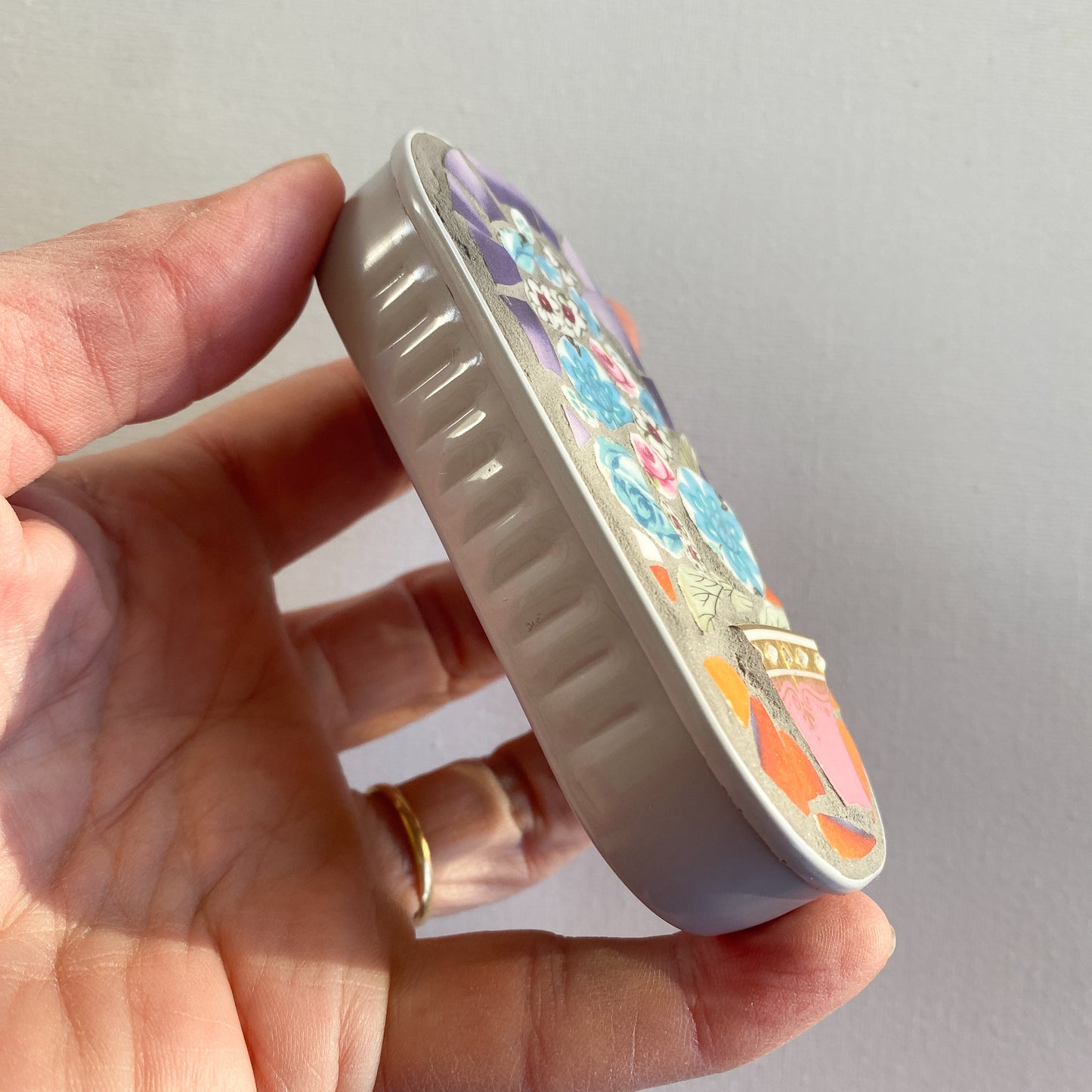 Hand holding a mosaic made in an anchovy can with a plain background