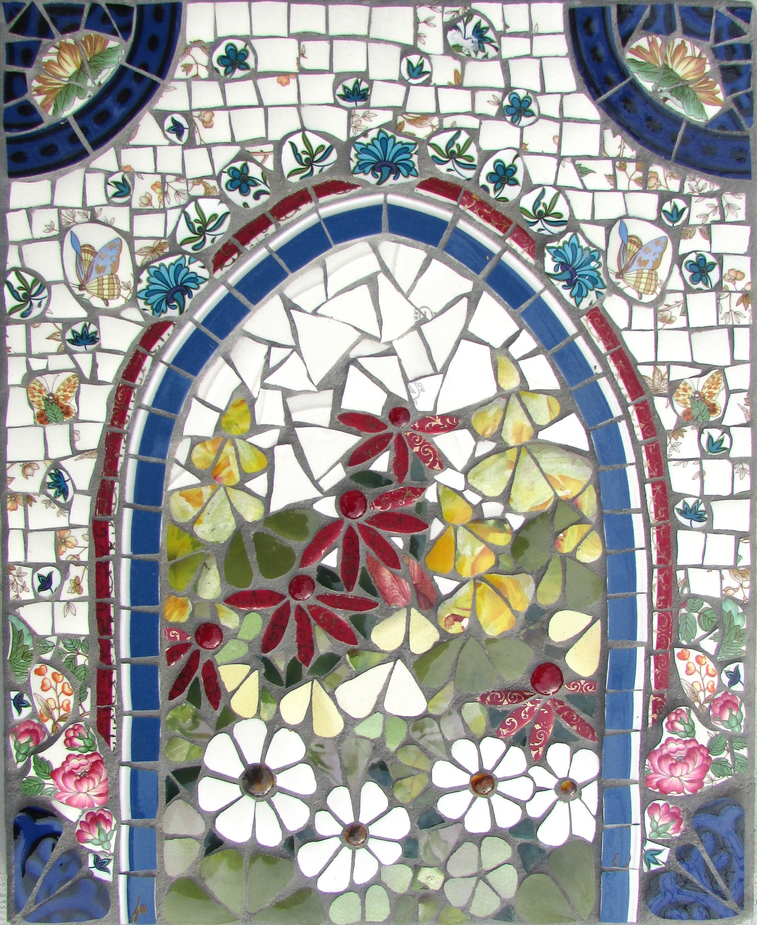 an arch in a wall, with a flower garden beyond, depicted in mosaic made from upcycled crockery