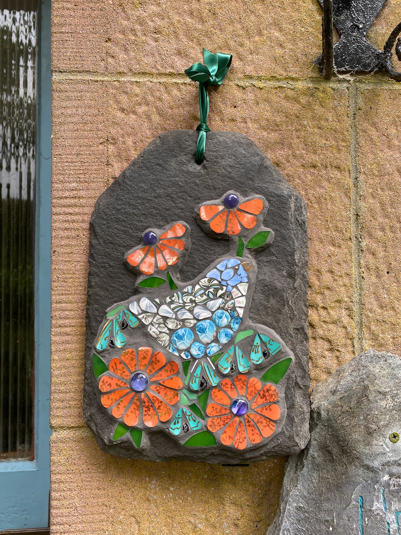 Decorative mosaic slate with flowers and a bird on a sandstone wall.