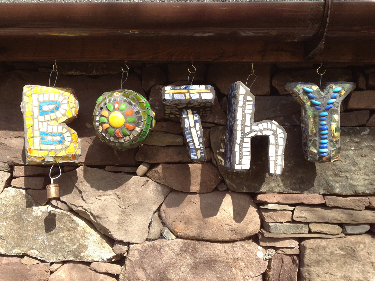 five hanging sculptural letters in mosaic, spelling Bothy