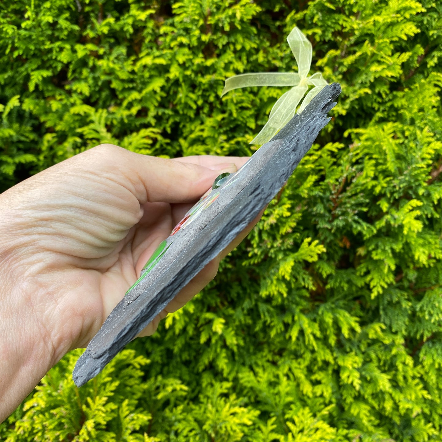 Hand holding a gray stone with greenery in the background