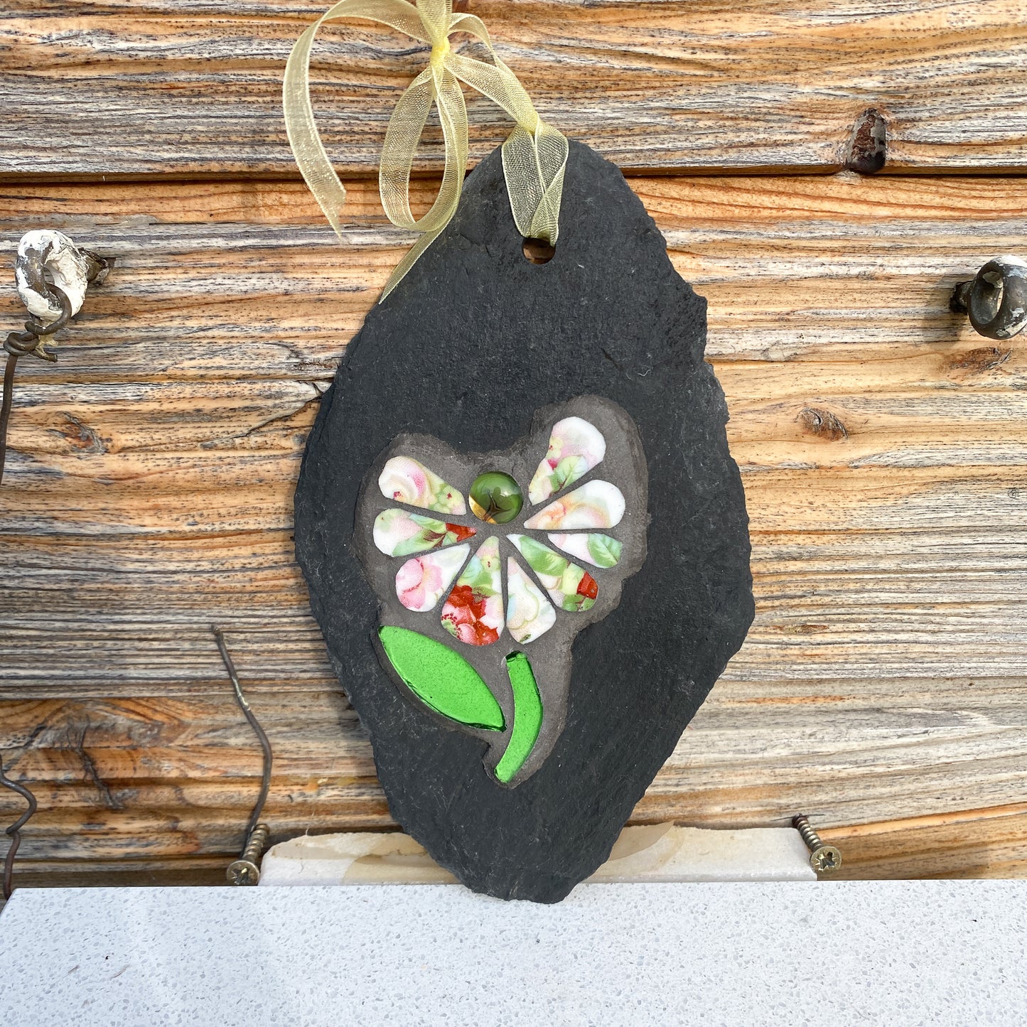 Decorative slate mosaic ornament with floral design photographed against a wooden surface