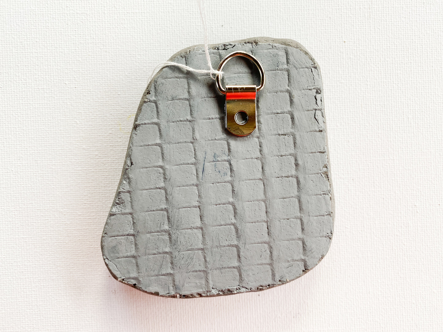 Gray textured kreverse side of mosaic with d-ring on a white background