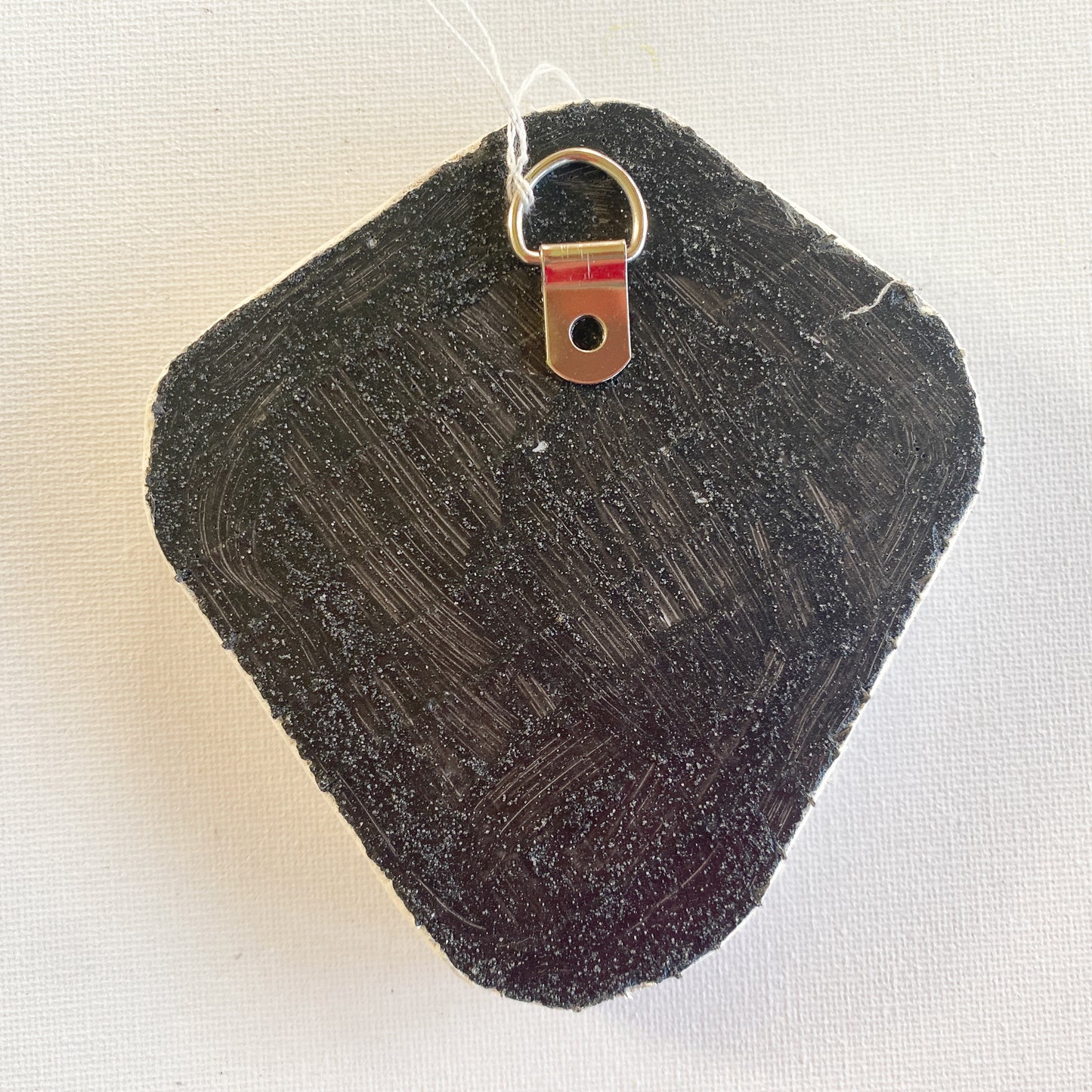 Black reverse side of a mosaic with a metal D-ring on a white background