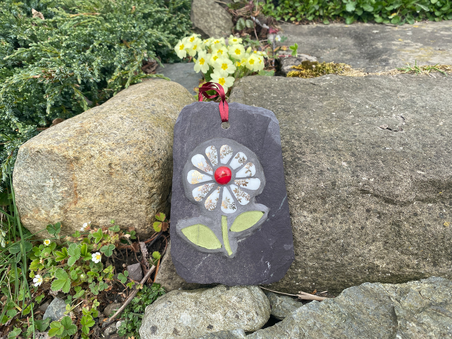 gilt and white petalled daisy mosaic on slate, shown on a drystone wall