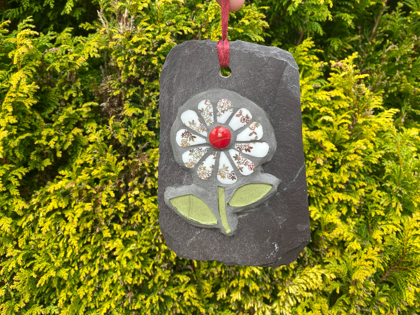 gilt and white petalled daisy mosaic on slate, with an evergreen tree behind