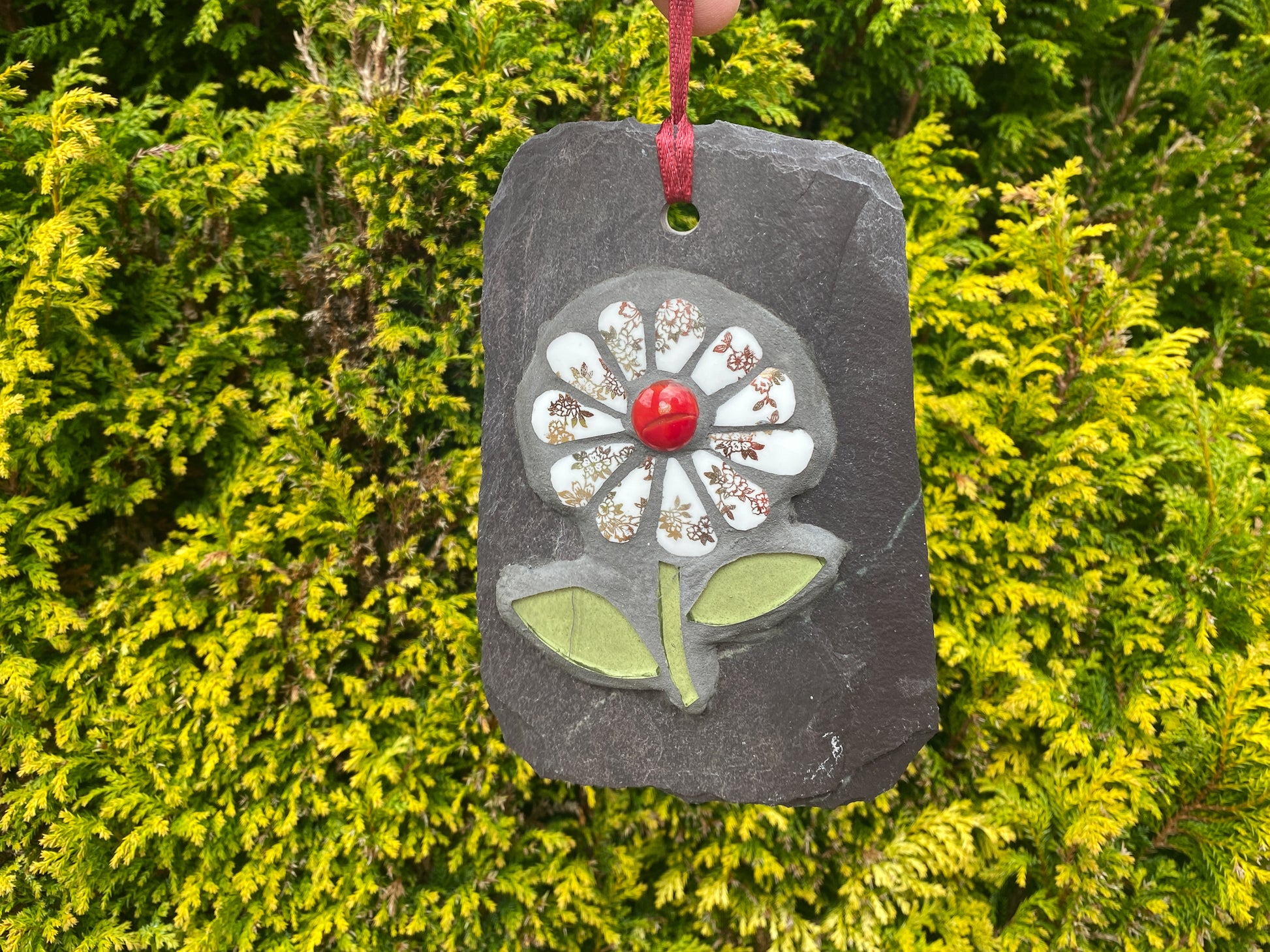 gilt and white petalled daisy mosaic on slate, with an evergreen tree behind