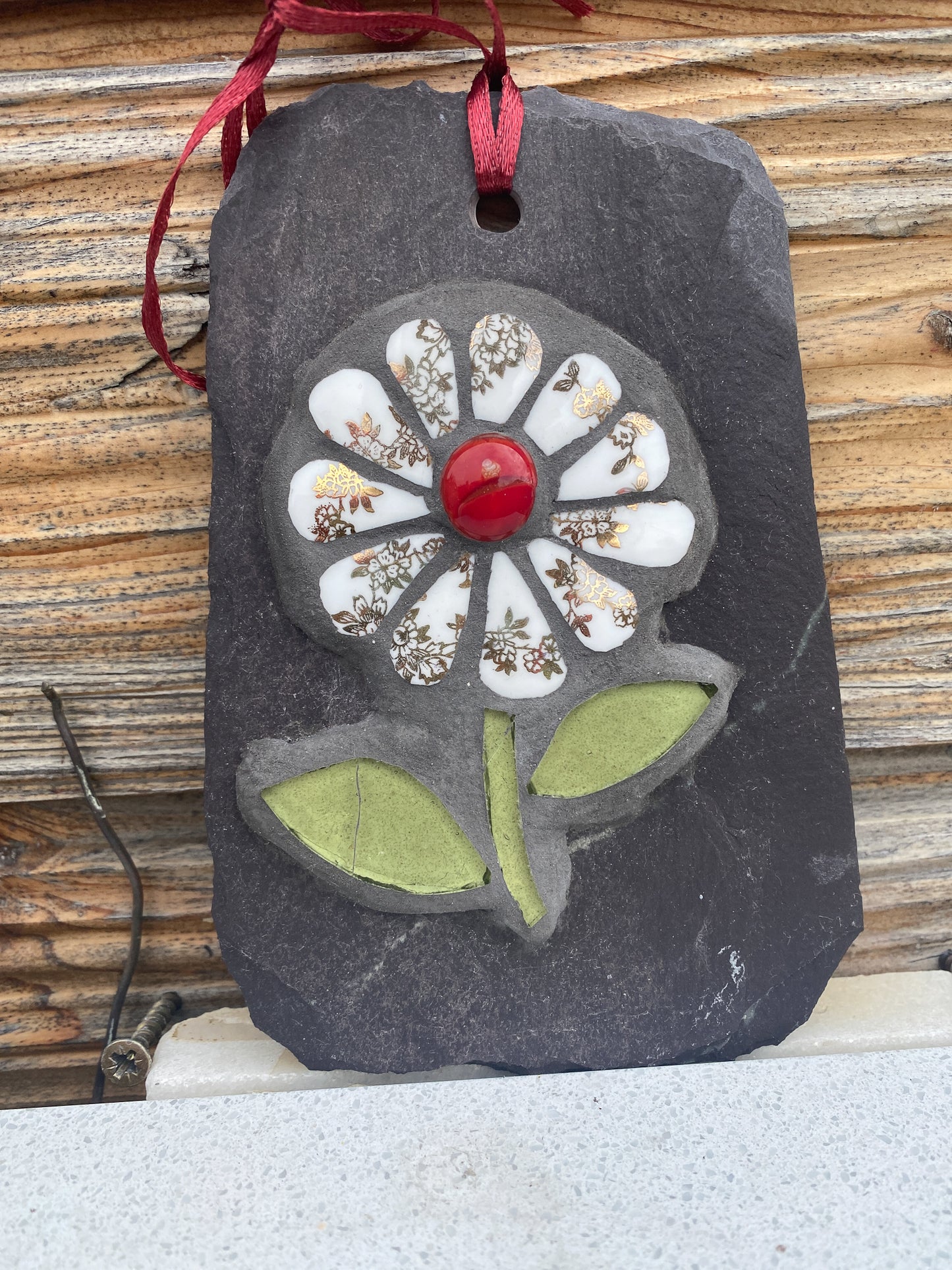 gilt and white petalled daisy mosaic on slate, shown on a marble surface with wooden shed behind