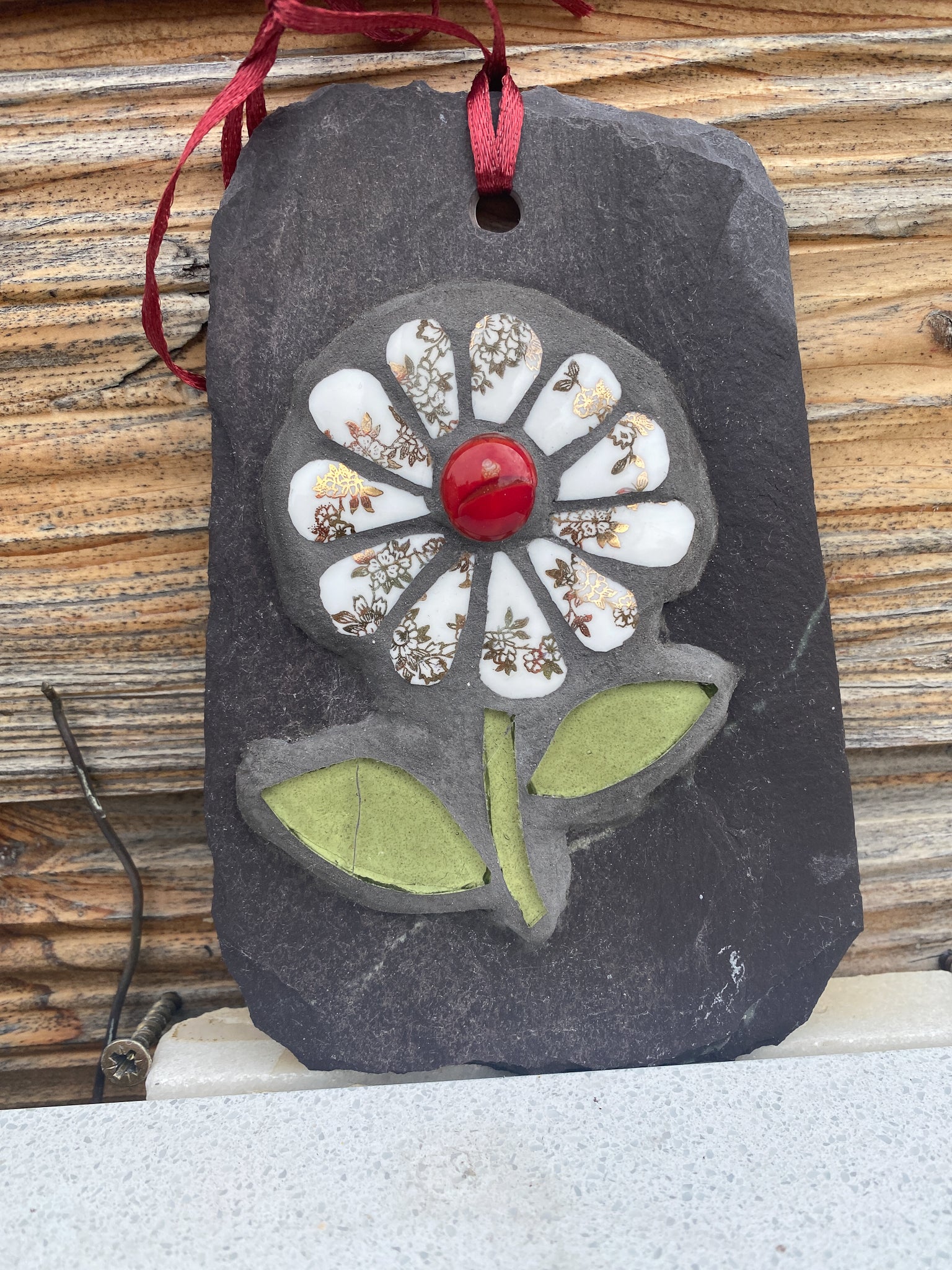 gilt and white petalled daisy mosaic on slate, shown on a marble surface with wooden shed behind