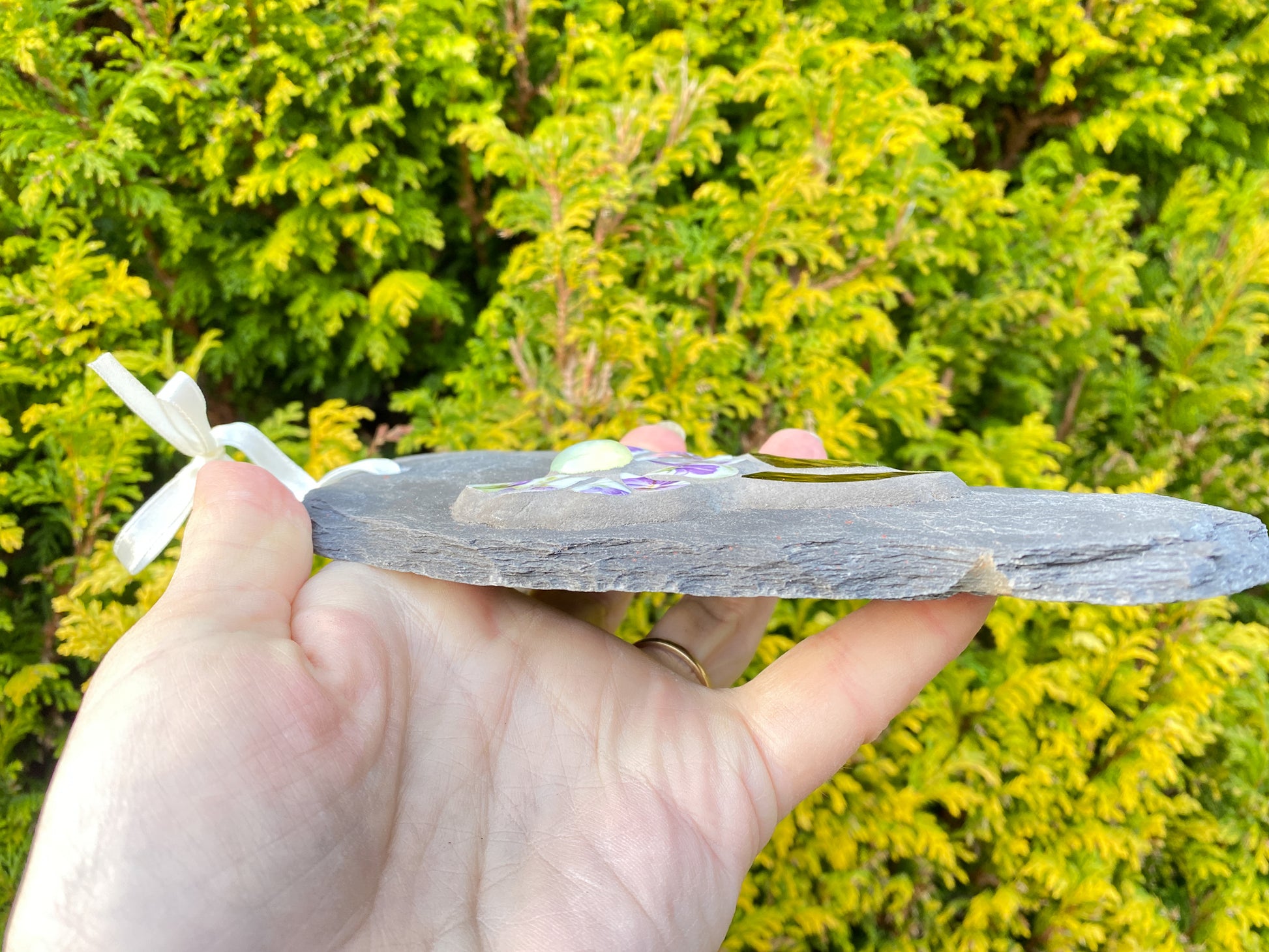 side of a slate, shown hand held, against an evergreen background