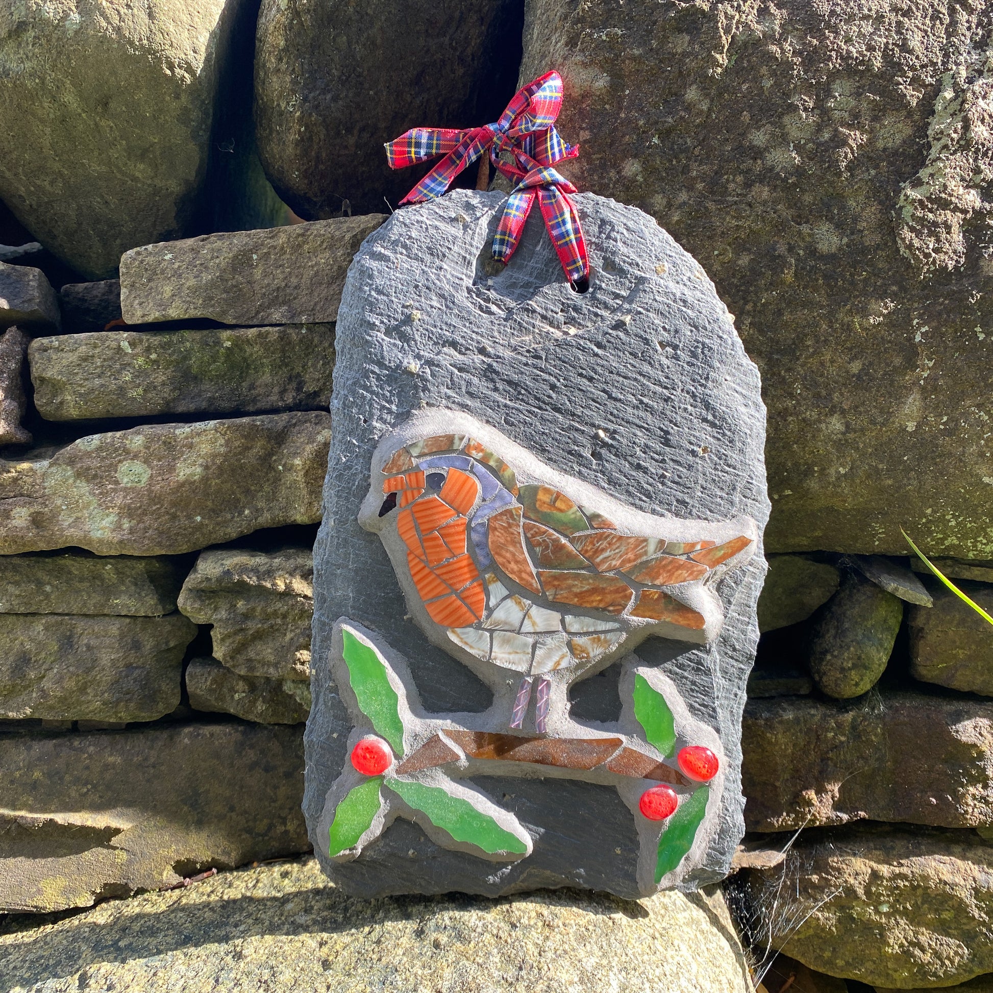 Decorative slate stone with mosaic robin design and red berries and green leaves against a stone wall background