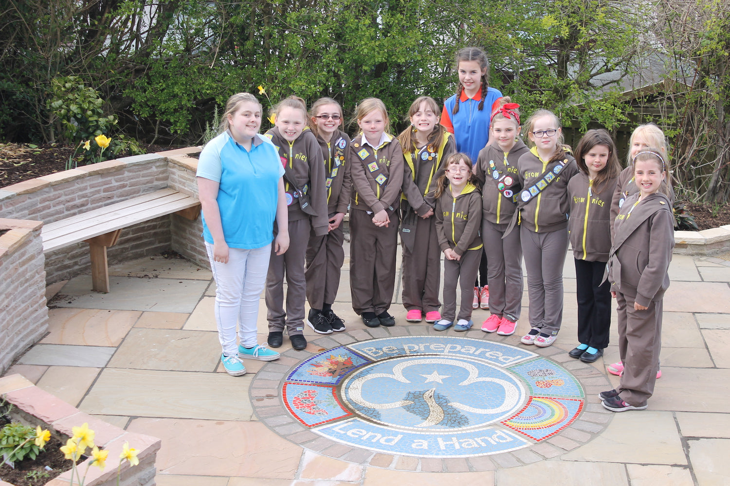 group of brownies on a patio, around a mosaic with guiding trefoil and wording saying Be Prepared Lend a Hand