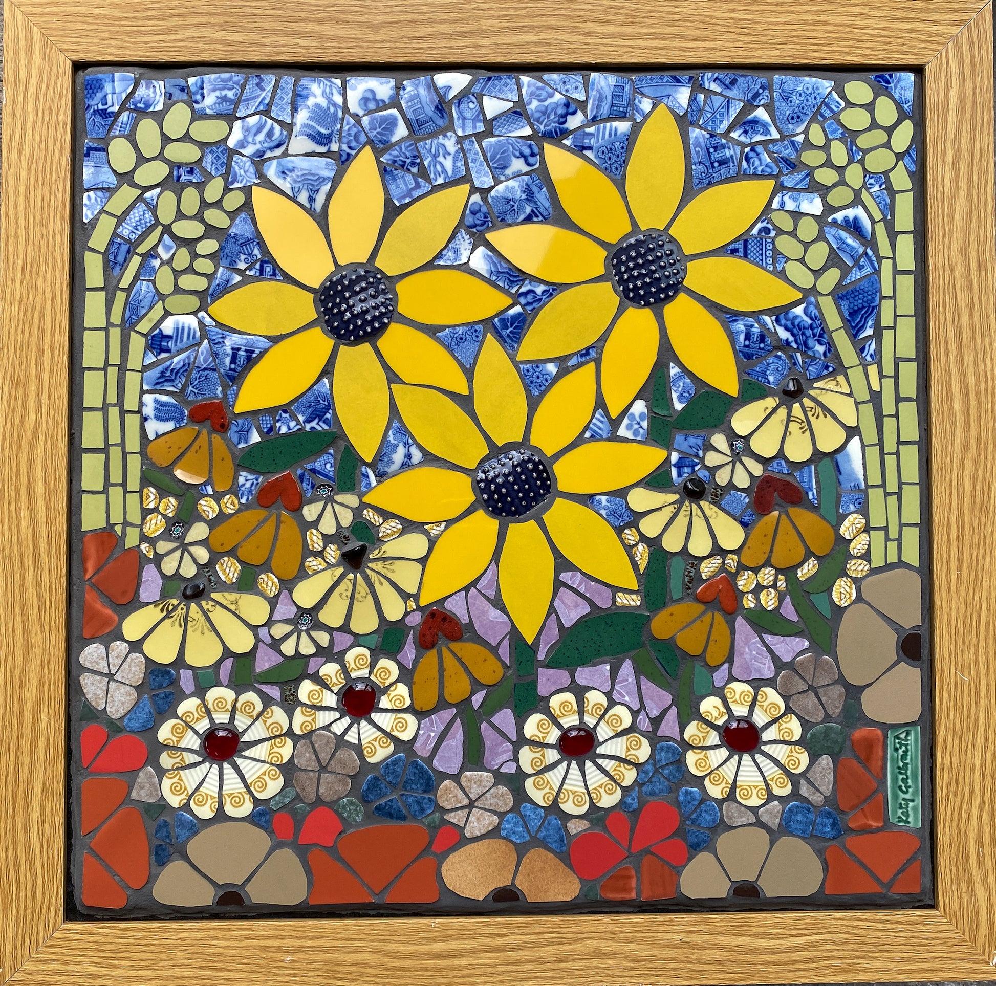 Mosaic artwork with yellow sunflowers, grasses and daisiy flowers and a wooden frame
