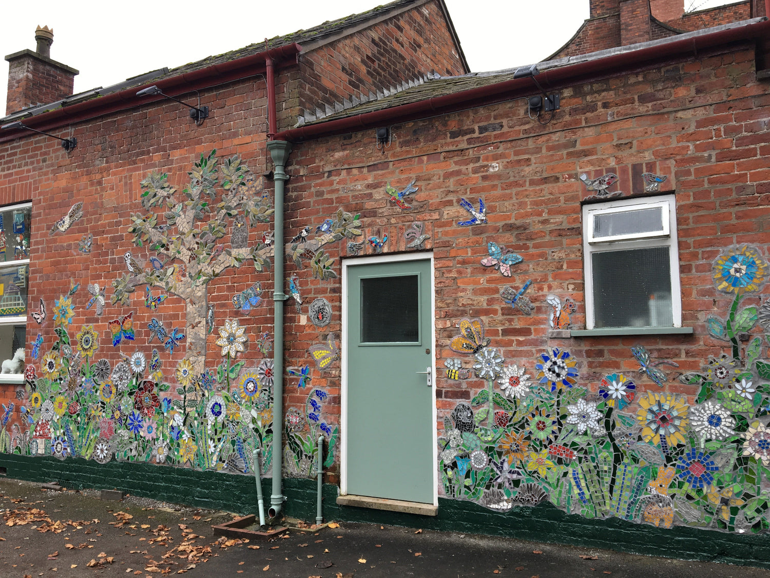 a flower garden and tree made in mosaic on a red brick wall