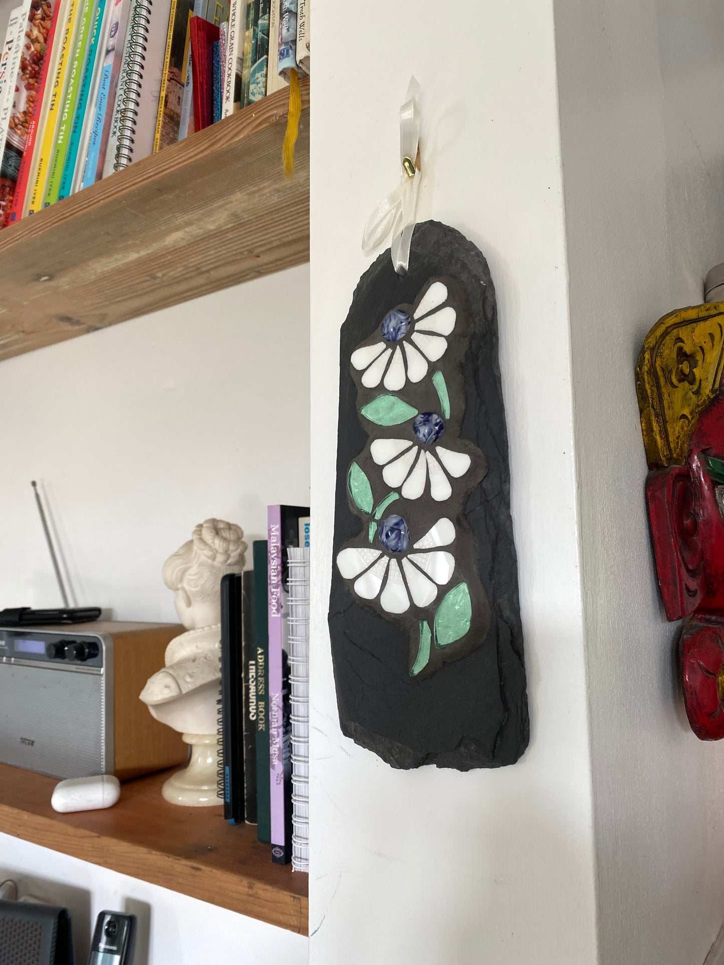Decorative slate with floral mosaic on a wall next to a shelf with books and a radio.