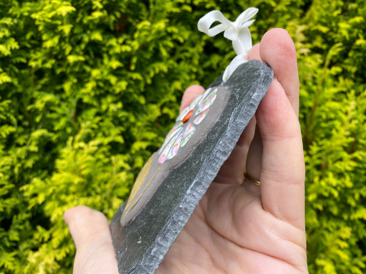 hand held slate at an angle, with a white flower and orange bead showing, against a foliage background