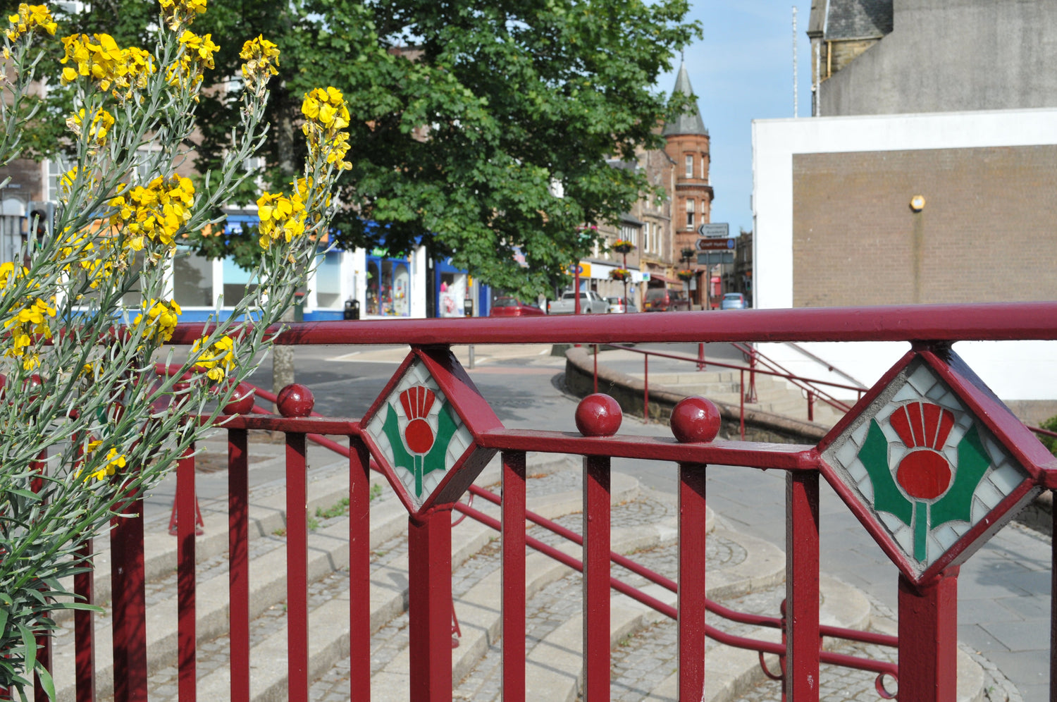 small thistle mosaics set into the red metal work surrounding a paved area in Crieff 